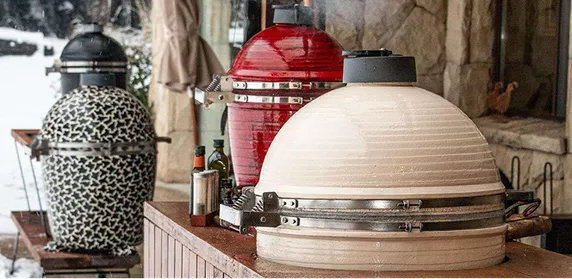 Drei Kamado B10 Grills mit Leoparden-Muster, in Rot und Cremeweiß auf einer verschneiten Terrasse