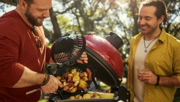 Zwei lächelnde Männer beim Auflegen von Kartoffeln auf einen Kamado Joe Grill