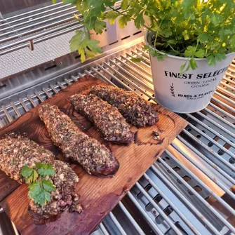 Four breaded steaks on a grill grate next to a pot with a parsley plant
