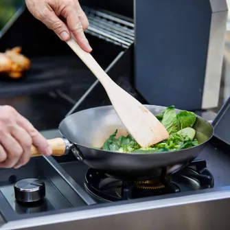 Green vegetables being cooked in a grill pan on a grill's cooking surface