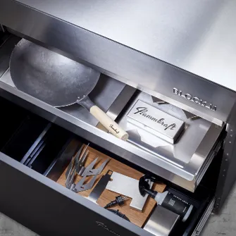Two open drawers of a Block M Flammkraft grill, containing various grilling utensils such as a pan