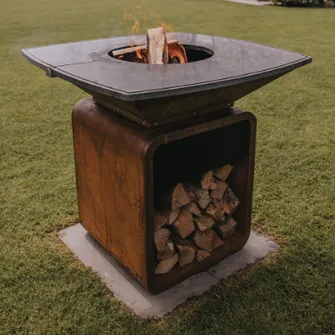 MOESTA One Grill with burning wood pieces, standing on a lawn