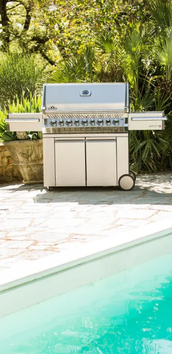 A Napoleon grill by a pool, surrounded by many tropical plants