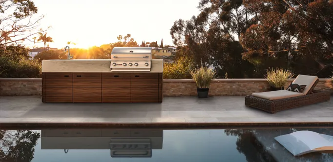 Luxurious OCQ outdoor kitchen by a pool with lounge chairs at sunset